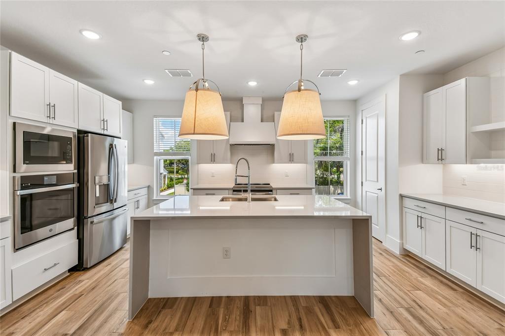 A modern kitchen features white cabinets, stainless steel appliances, a large island, and wood flooring — 202 PASQUALA, OVIEDO, FL