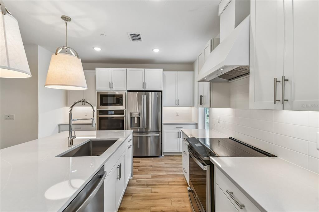 A modern kitchen features white cabinetry, stainless steel appliances, a large island, and wood flooring — 202 PASQUALA, OVIEDO, FL