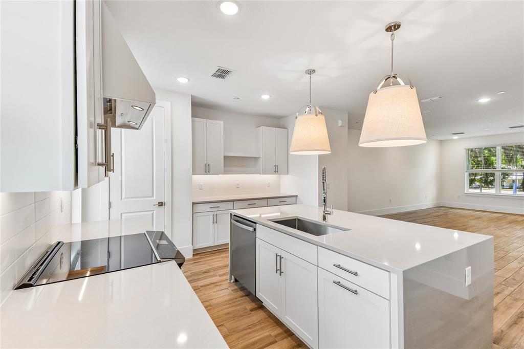 A modern kitchen features white cabinets, quartz countertops, a center island, and wood-look flooring — 202 PASQUALA, OVIEDO, FL