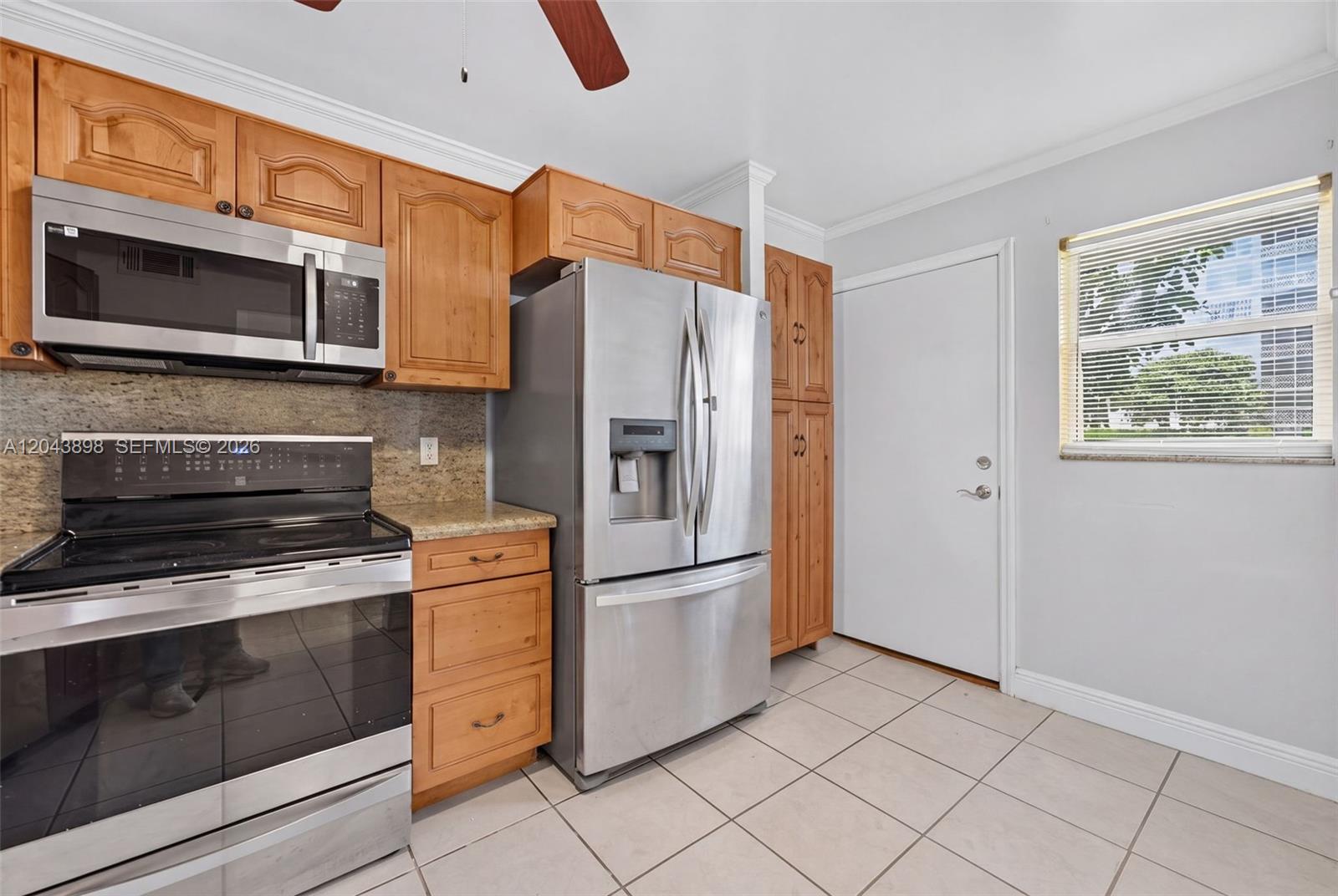 A kitchen features wood cabinets, stainless steel appliances, granite countertops, and light-colored tile flooring — 1780 NE 191st St # 2, North Miami FL 33179, NORTH MIAMI, FL