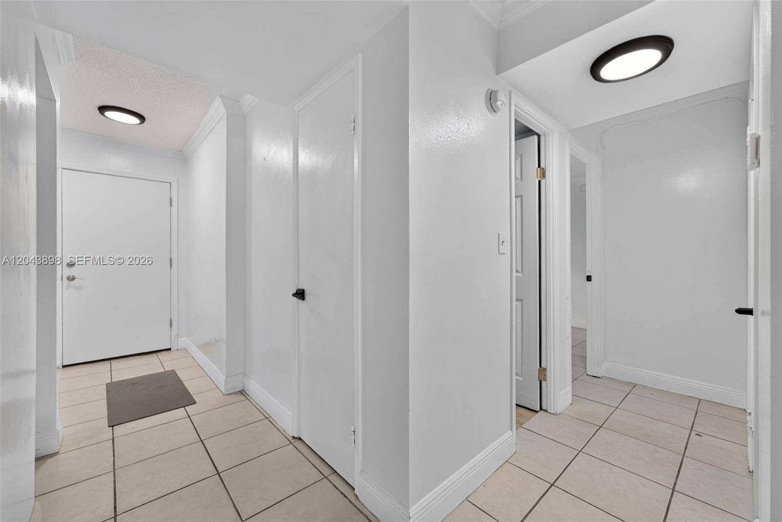 A hallway with white walls, tiled floors, and multiple closed doors under two ceiling lights — 1780 NE 191st St # 2, North Miami FL 33179, NORTH MIAMI, FL