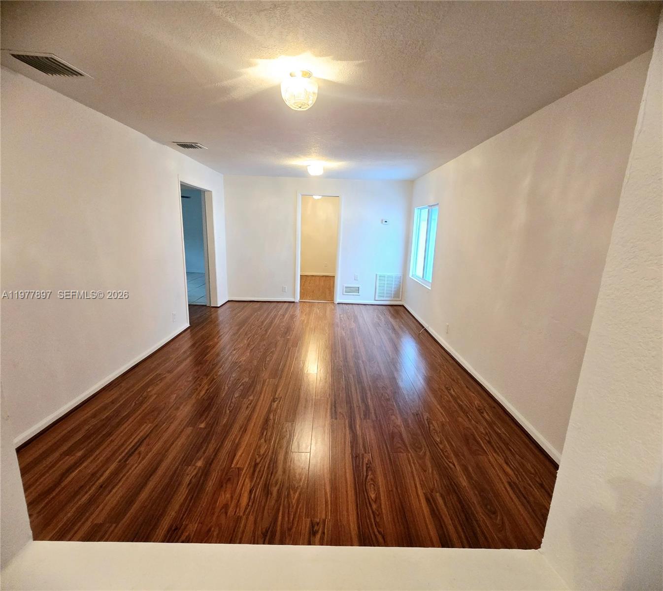An empty room features white walls, dark wood-look flooring, and two ceiling light fixtures — 1436 NW 51st Ter, Miami FL 33142, MIAMI, FL