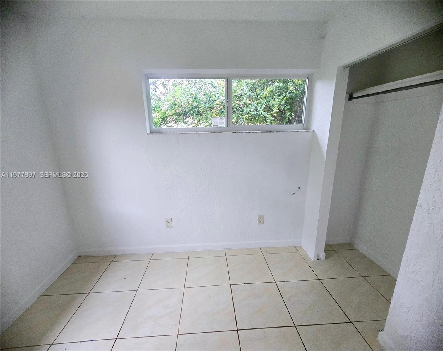 A small, empty room features white walls, tiled flooring, a horizontal window, and a closet — 1436 NW 51st Ter, Miami FL 33142, MIAMI, FL