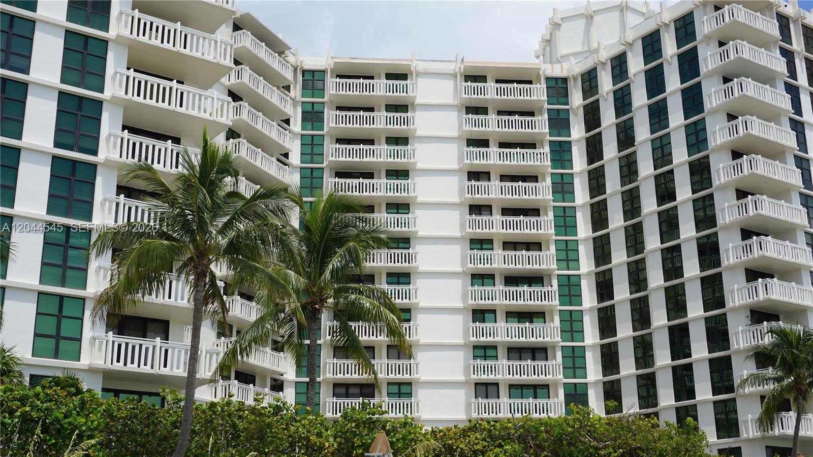 A multi-story white condominium building features numerous balconies and large windows behind palm trees — 1111 Crandon Blvd # B705, Key Biscayne FL 33149, KEY BISCAYNE, FL