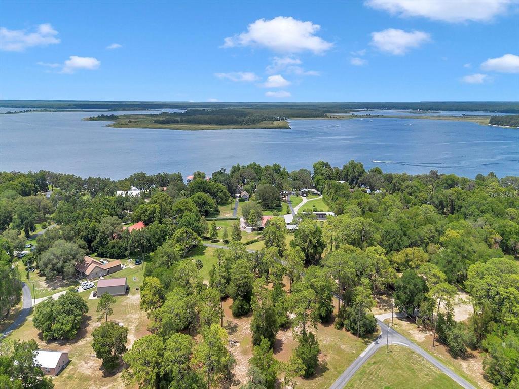 An aerial view shows a wooded property with several buildings situated along a large lake — 23608 NE 124TH PLACE ROAD, FORT MC COY, FL
