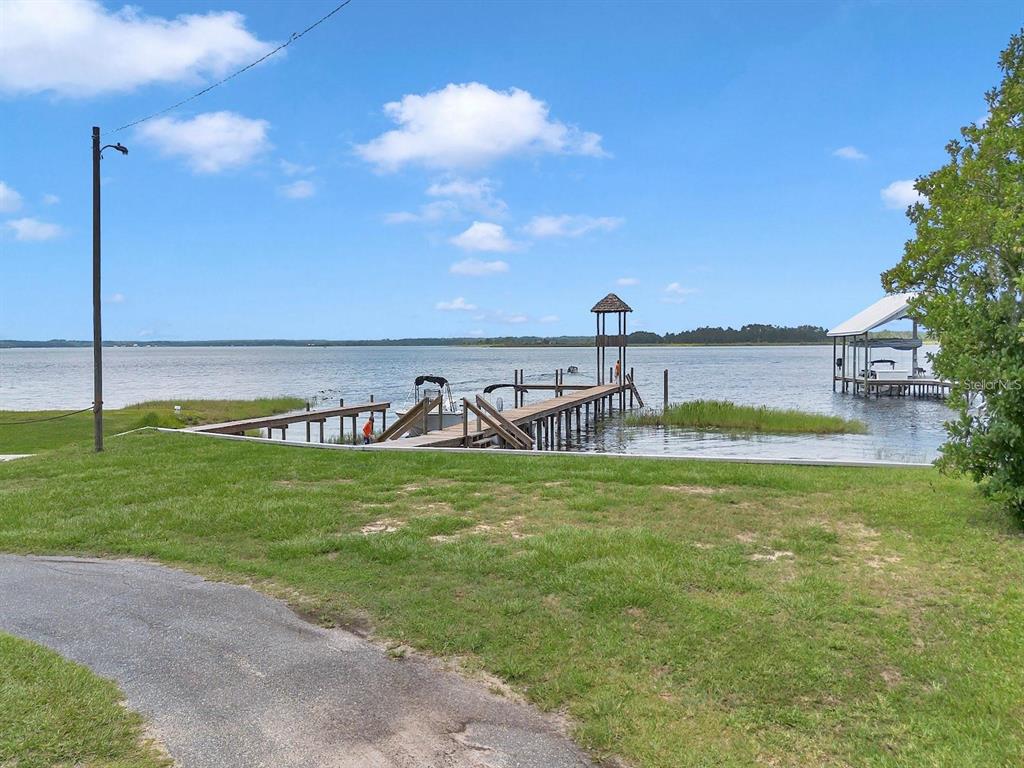 A wooden dock with a covered gazebo extends into a large lake from a lawn — 23608 NE 124TH PLACE ROAD, FORT MC COY, FL