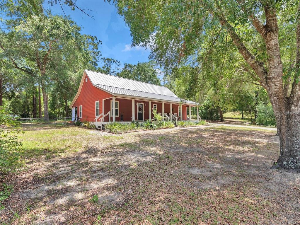 A red house with a metal roof and a front porch sits in a wooded yard — 23608 NE 124TH PLACE ROAD, FORT MC COY, FL