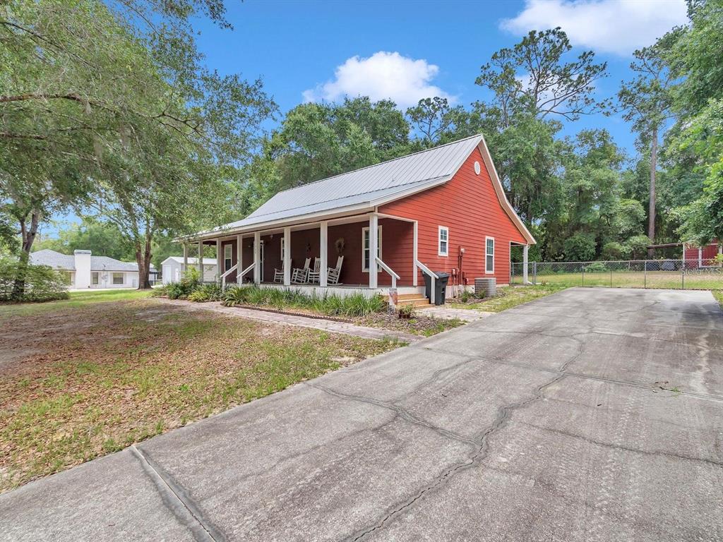 A red house with a metal roof and a front porch sits beside a driveway — 23608 NE 124TH PLACE ROAD, FORT MC COY, FL