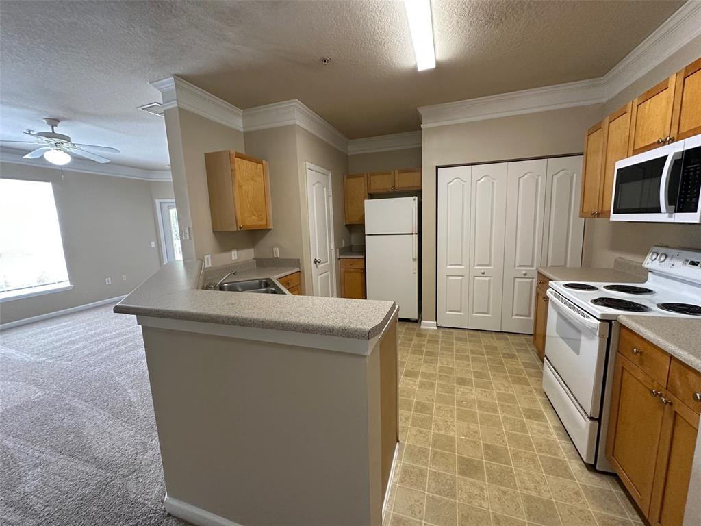 A kitchen with light wood cabinets, white appliances, and a breakfast bar overlooking a carpeted room — 8836 VILLA VIEW CIRCLE UNIT 201, ORLANDO, FL