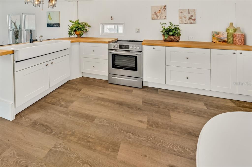 A kitchen features white cabinets, butcher block countertops, a farmhouse sink, and wood-look flooring — 10921 LONDON DRIVE, PORT RICHEY, FL