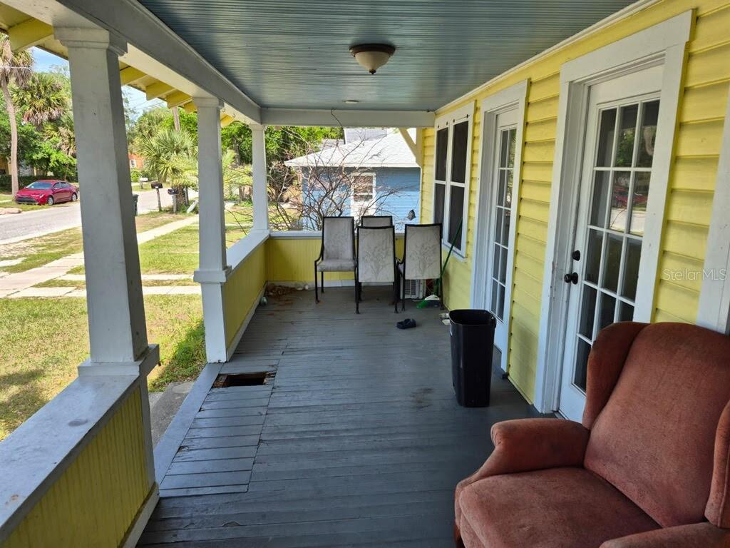 A covered front porch with yellow siding, a gray wooden floor, and several chairs — 219 NORTH STREET, DAYTONA BEACH, FL