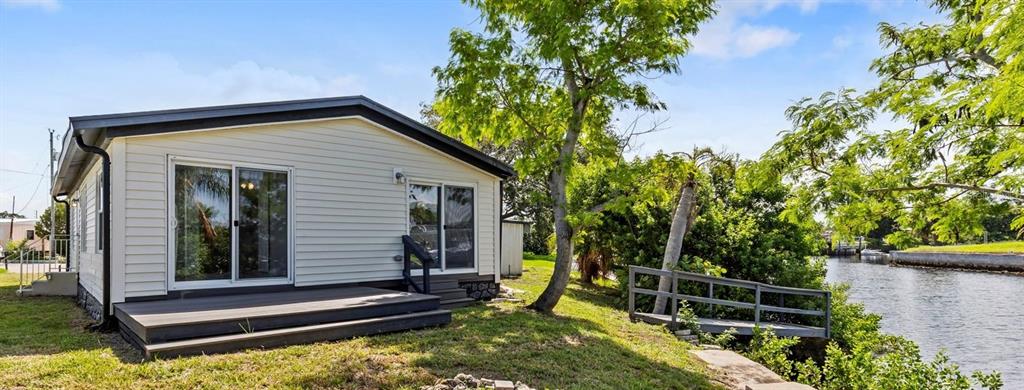 A light-colored mobile home with a wooden deck sits beside a canal — 13147 CABIN COURT, HUDSON, FL