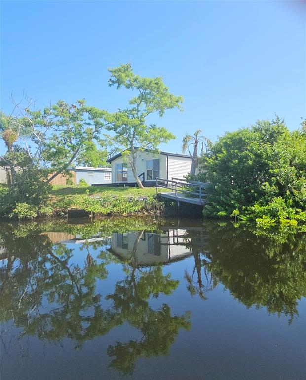 A white mobile home sits on a grassy bank overlooking a calm canal — 13147 CABIN COURT, HUDSON, FL