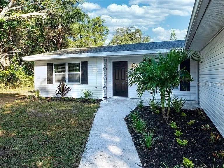 A white single-story house with a black front door and a palm tree in front — 120 AVENIDA DE BAHA, NOKOMIS, FL