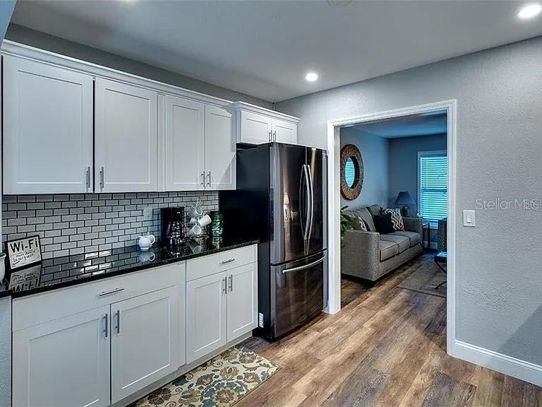 A kitchen with white cabinets, black countertops, and a stainless steel refrigerator leads into a living room — 120 AVENIDA DE BAHA, NOKOMIS, FL