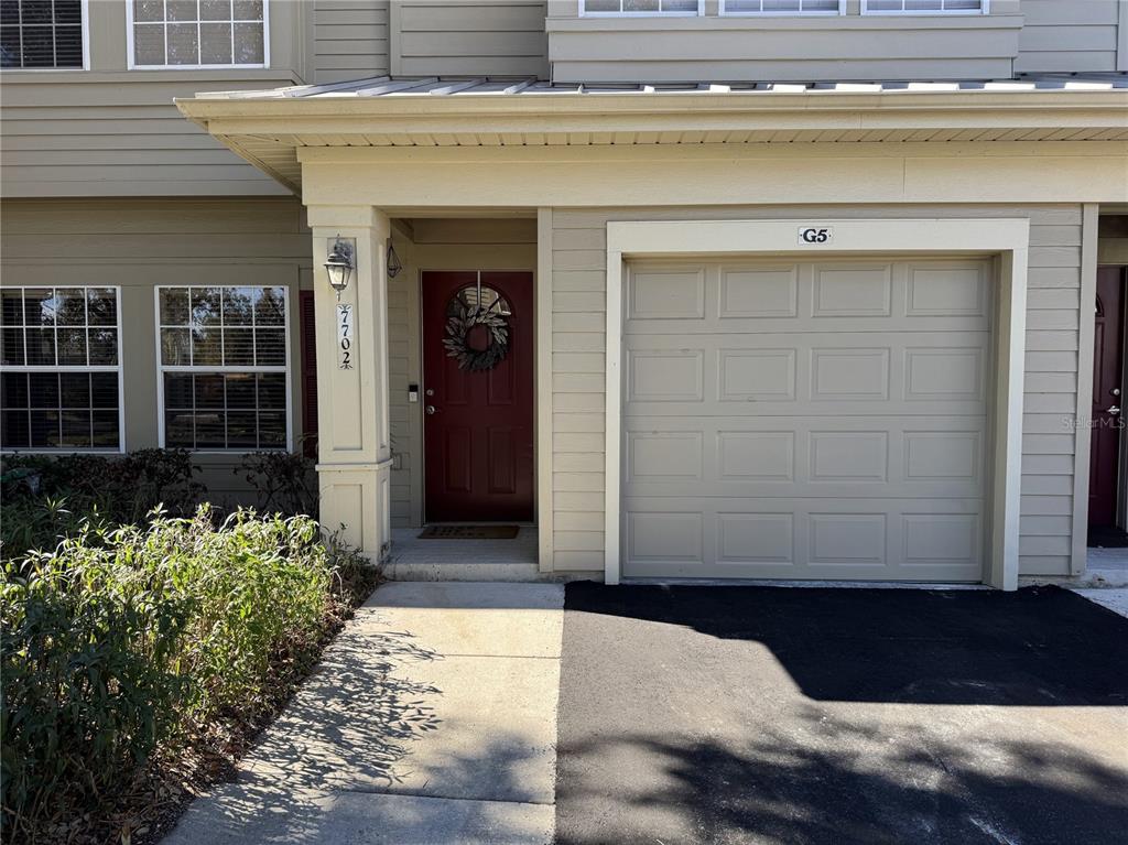 A tan townhouse exterior features a red front door, a garage, and a concrete walkway — 7702 PLANTATION CIRCLE, BRADENTON, FL