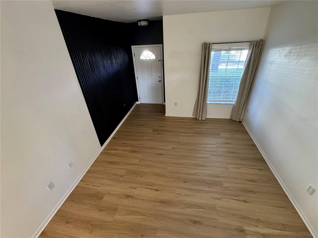 An empty room features light wood-look flooring, white walls, and a black accent wall — 7702 PLANTATION CIRCLE, BRADENTON, FL