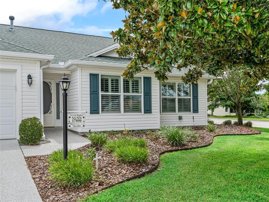 A single-story house with white siding, dark shutters, and a landscaped front yard — 17899 SE 87TH BOURNE AVENUE, THE VILLAGES, FL