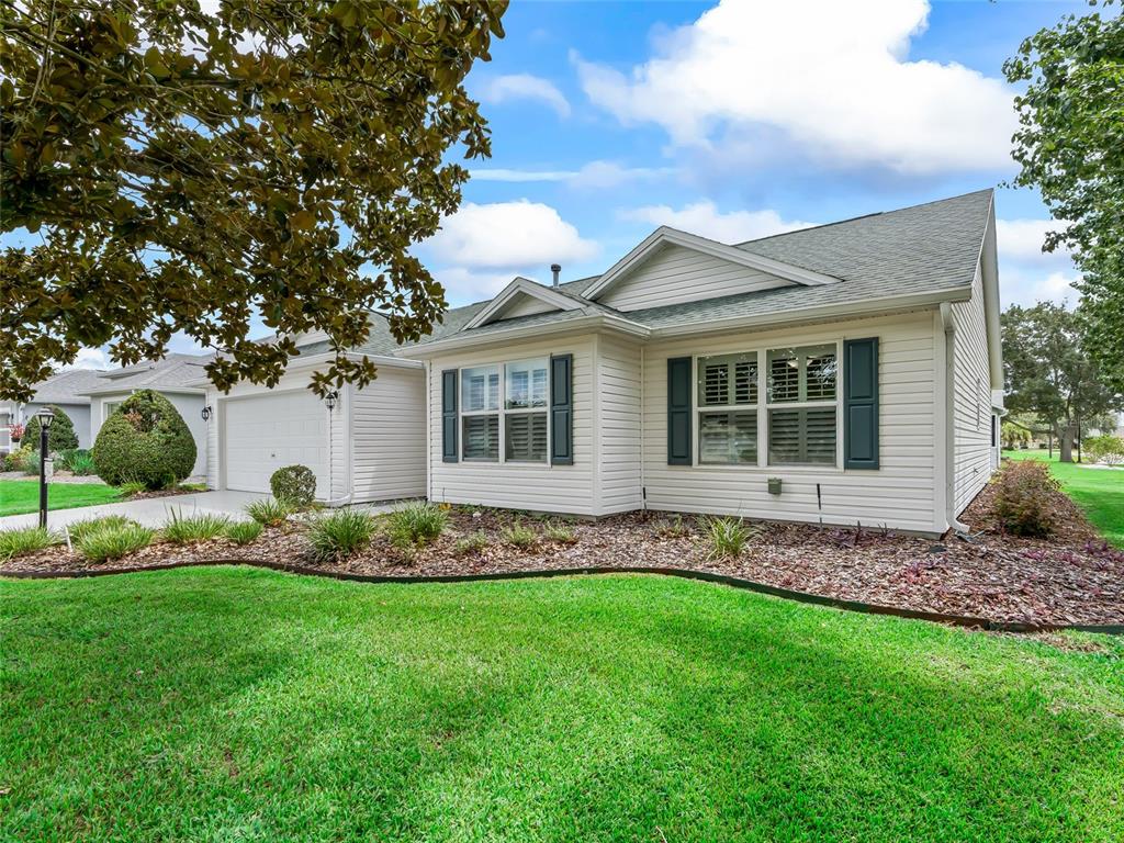 A single-story house with white vinyl siding, dark shutters, and a landscaped front yard — 17899 SE 87TH BOURNE AVENUE, THE VILLAGES, FL