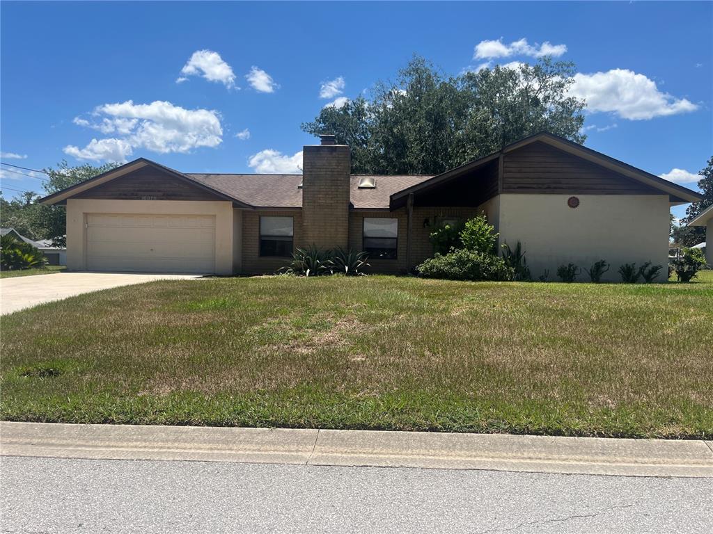 A single-story house with a tan stucco exterior, brick chimney, and attached two-car garage — 10878 SE 45TH AVENUE, BELLEVIEW, FL