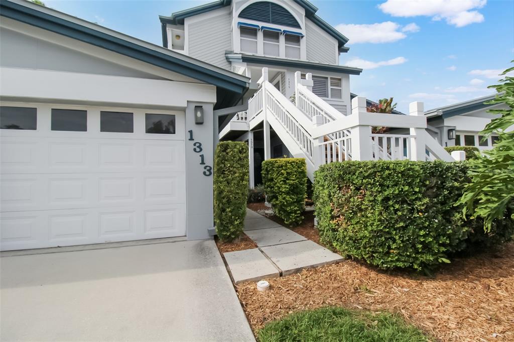 A two-story house features a white garage, a staircase leading to the entrance, and landscaping — 1313 SIESTA BAYSIDE DRIVE UNIT 1313-D, SARASOTA, FL