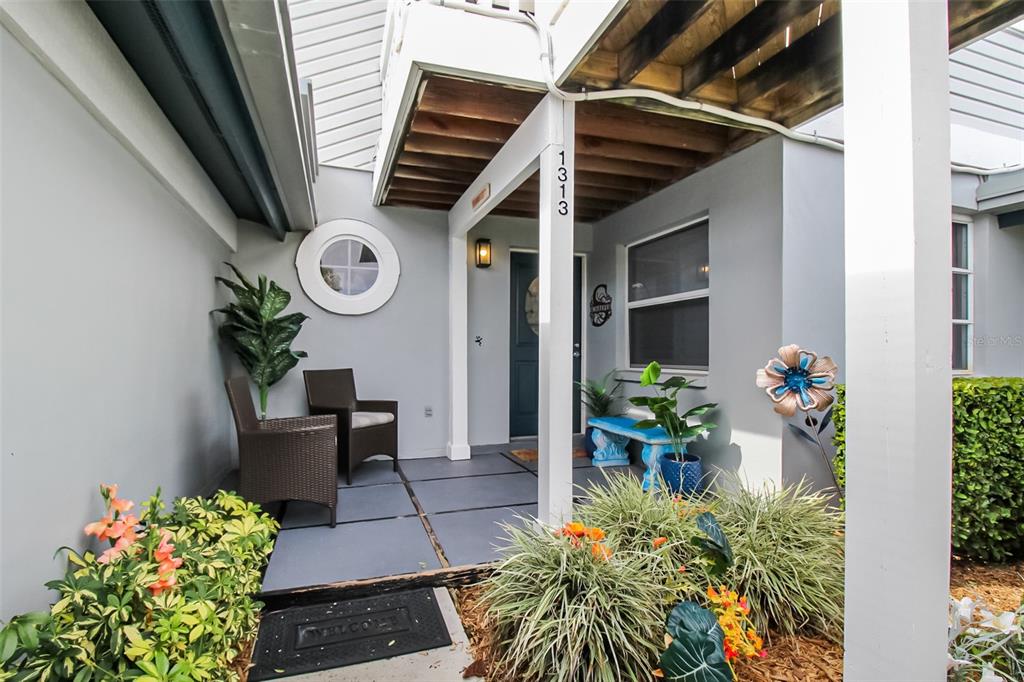 A covered front porch features gray tiled flooring, two wicker chairs, and a blue bench — 1313 SIESTA BAYSIDE DRIVE UNIT 1313-D, SARASOTA, FL