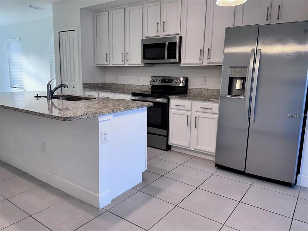 A kitchen features white cabinets, granite countertops, stainless steel appliances, and a central island — 4774 TERRA ESMERALDA DRIVE, KISSIMMEE, FL
