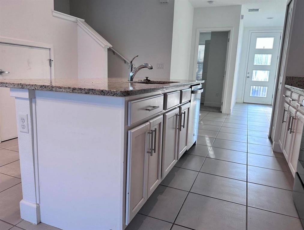 A kitchen island with a granite countertop and sink sits on a tiled floor — 4774 TERRA ESMERALDA DRIVE, KISSIMMEE, FL