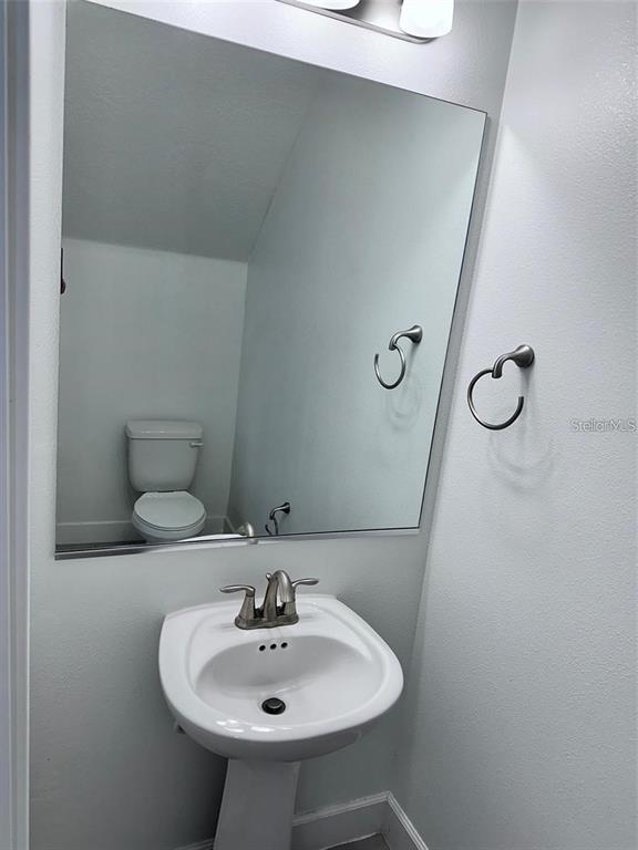 A small bathroom features a white pedestal sink, a toilet, and a large wall mirror — 4774 TERRA ESMERALDA DRIVE, KISSIMMEE, FL