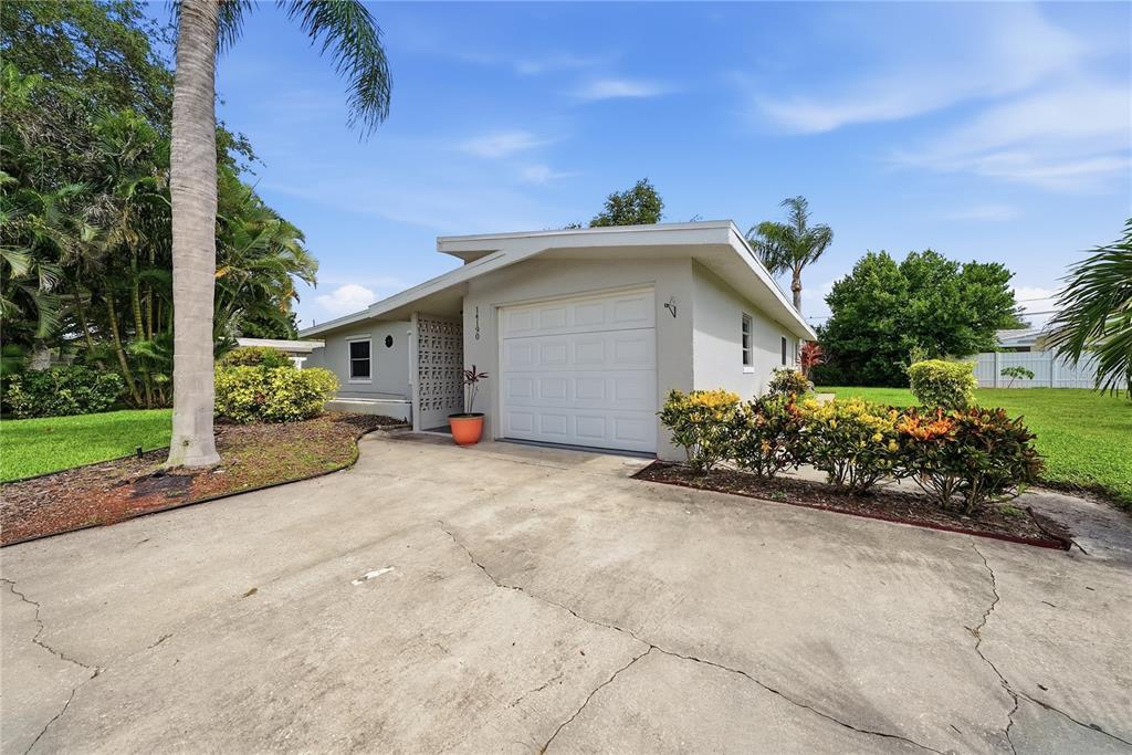 A single-story house with a white garage door, concrete driveway, and surrounding tropical landscaping — 14190 PAGE AVENUE, LARGO, FL