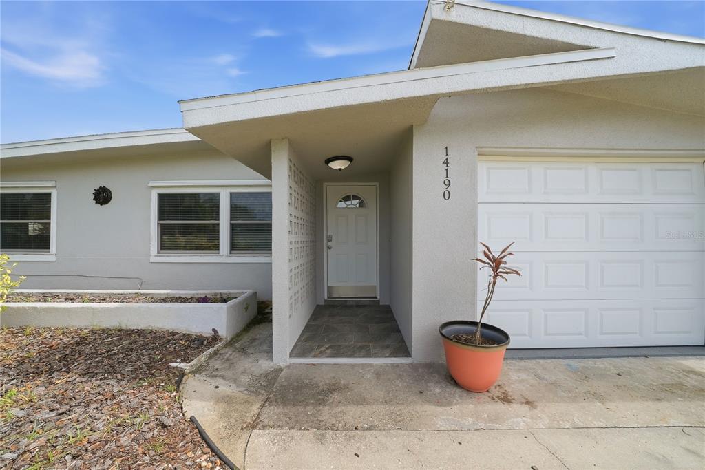 The exterior of a house features a white front door, a garage, and a potted plant — 14190 PAGE AVENUE, LARGO, FL