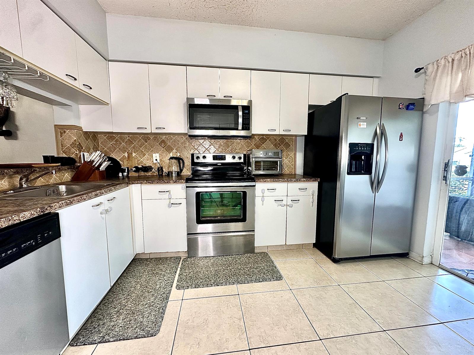 A kitchen features white cabinetry, stainless steel appliances, a tiled backsplash, and light-colored floor tiles — 5336 Jubilee Way # 189, Margate FL 33063, MARGATE, FL
