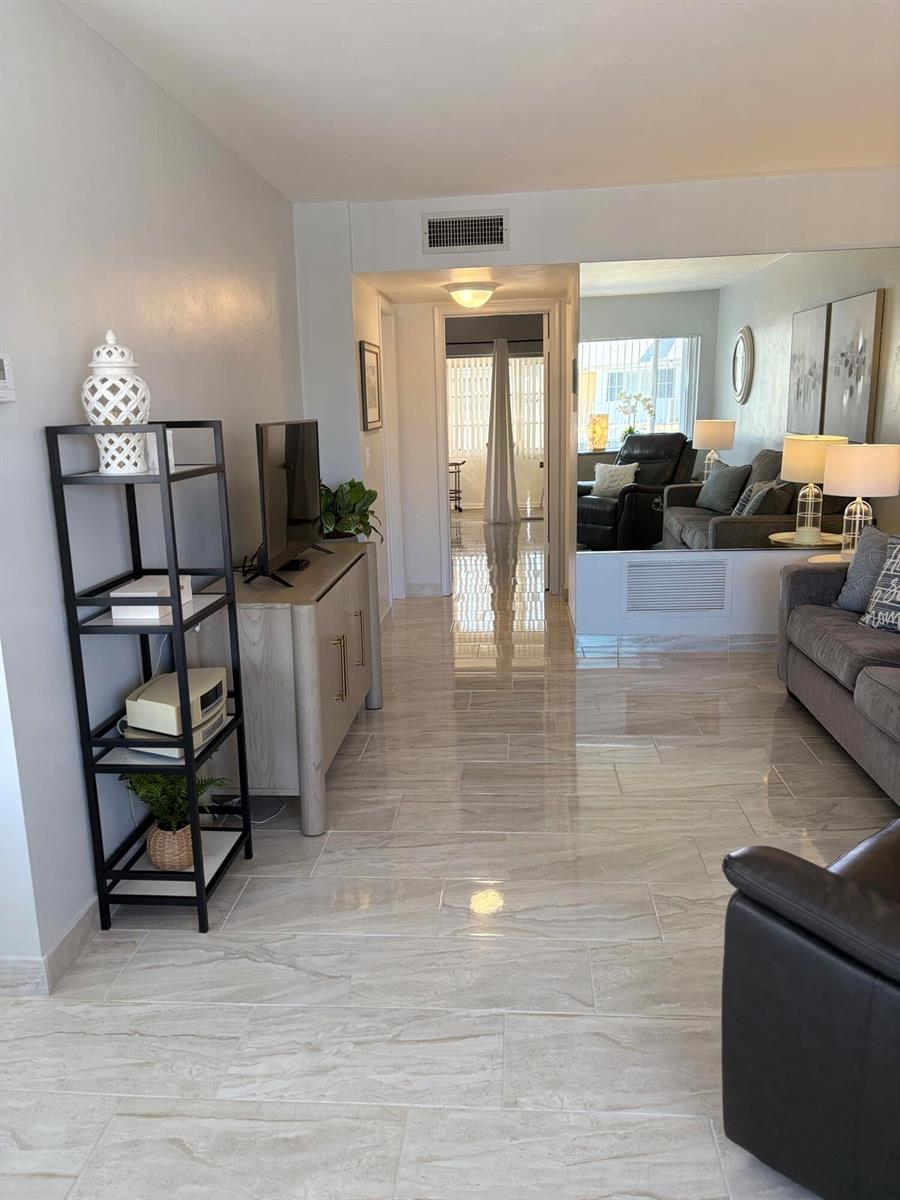 A living room with light tile flooring, a black metal shelving unit, and a mirrored wall — 3280 Lake Osborne Drive # 206, FL 33461, FL