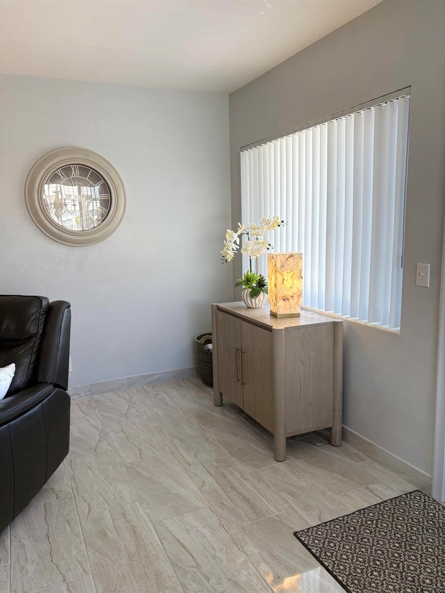 A living room features light-colored tile flooring, a wooden cabinet, a wall clock, and vertical blinds — 3280 Lake Osborne Drive # 206, FL 33461, FL