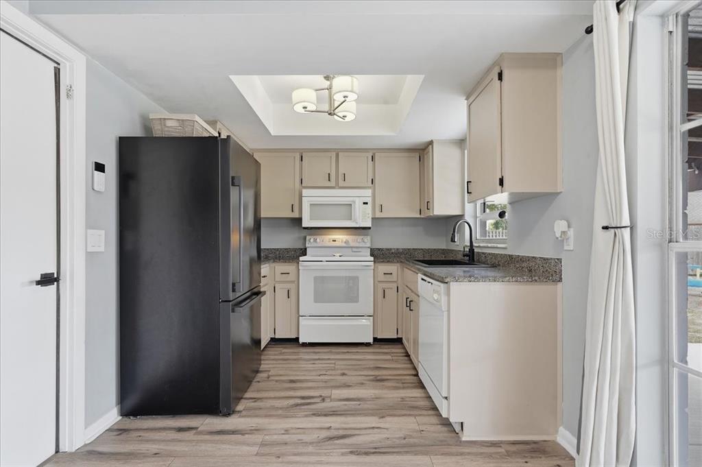 A kitchen features light-colored cabinets, granite countertops, a black refrigerator, and wood-look flooring — 8913 WOOD LAKE COURT, NEW PORT RICHEY, FL
