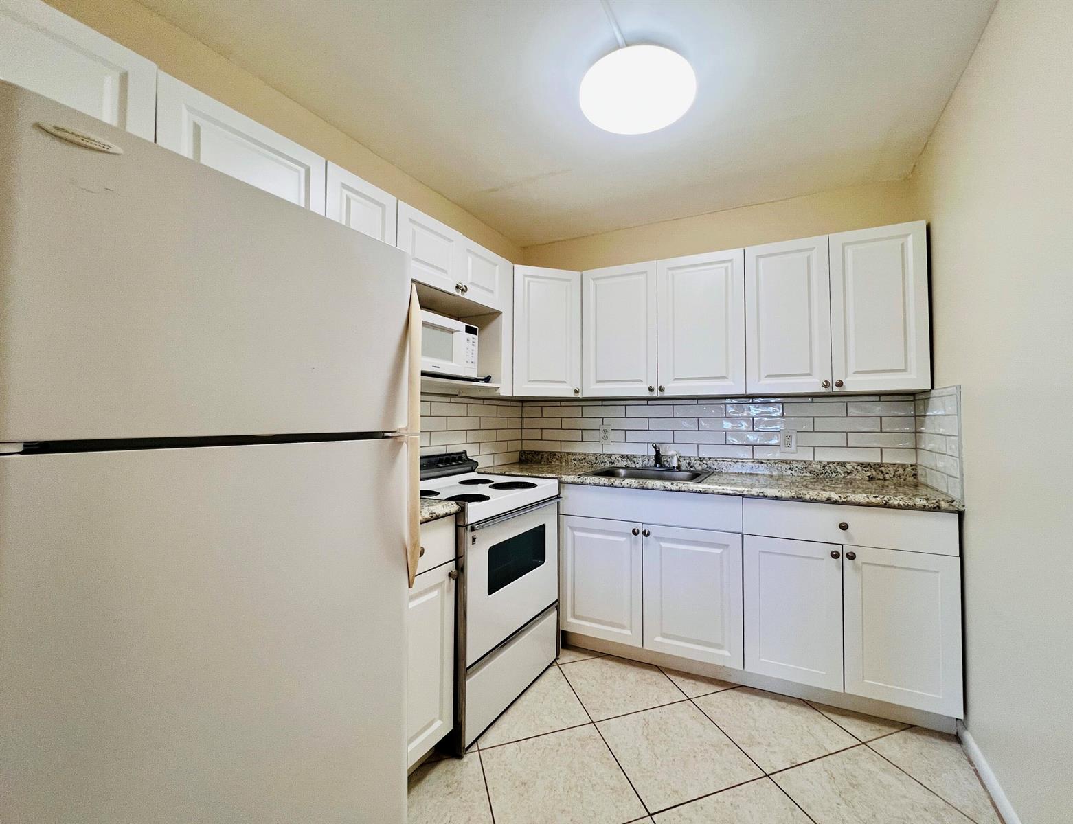 A kitchen features white cabinets, a white stove, a refrigerator, and a tiled backsplash — 27 Sheffield B, West Palm Beach FL 33417, WEST PALM BEACH, FL