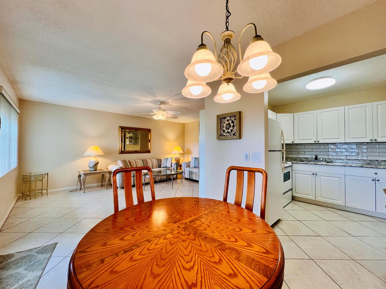 A dining area with a wooden table and chandelier opens into a living room and kitchen — 27 Sheffield B, West Palm Beach FL 33417, WEST PALM BEACH, FL