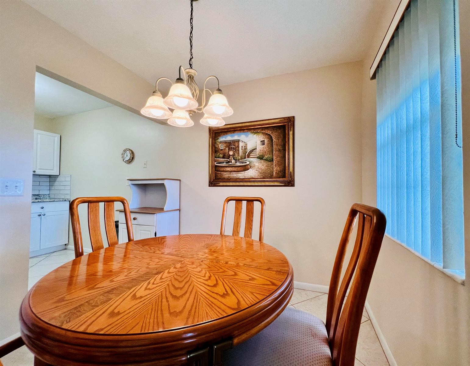 A dining area features a round wooden table, three chairs, a chandelier, and wall art — 27 Sheffield B, West Palm Beach FL 33417, WEST PALM BEACH, FL