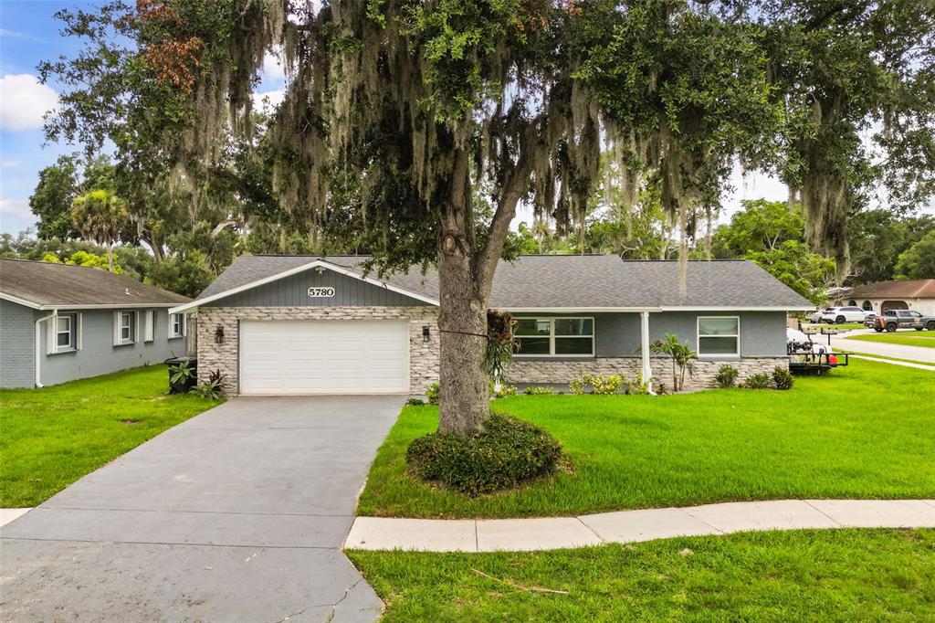 A single-story house with a gray exterior, stone accents, a two-car garage, and a large tree — 5780 DEVON STREET, PORT ORANGE, FL