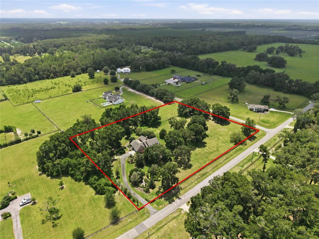 An aerial view shows a house situated on a large, tree-filled lot outlined in red — 26341 NW 166TH AVENUE, HIGH SPRINGS, FL