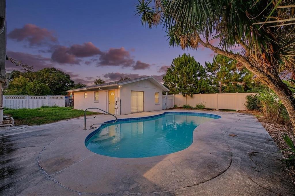 A backyard swimming pool sits in front of a small white detached building at dusk — 1647 SUMMERDALE DRIVE S, CLEARWATER, FL