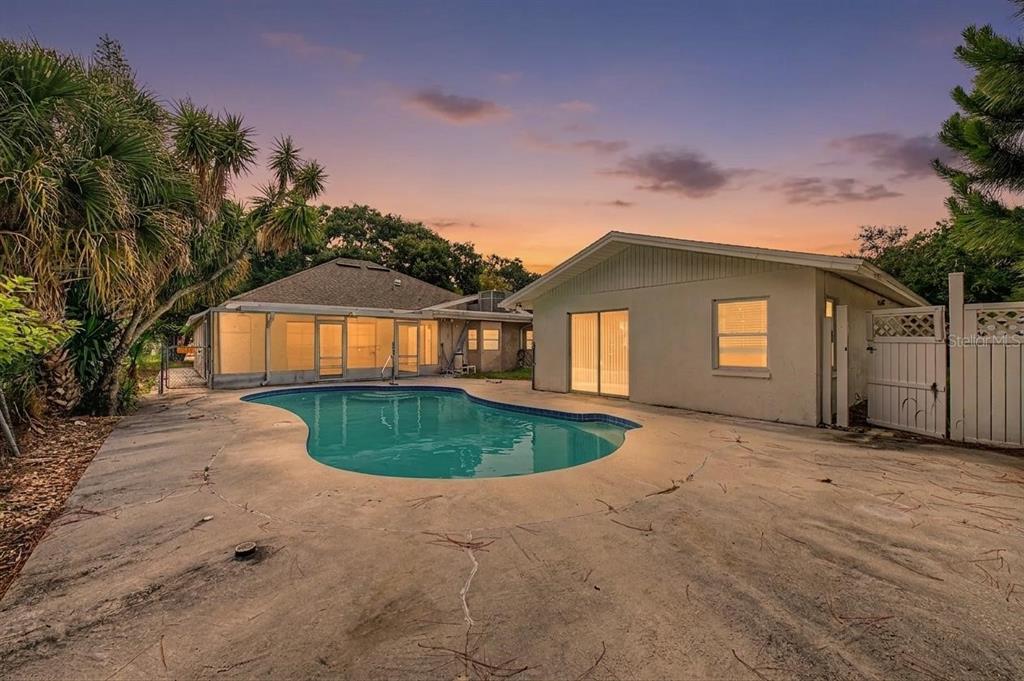 A backyard features a swimming pool, a concrete patio, and a house with a screened porch — 1647 SUMMERDALE DRIVE S, CLEARWATER, FL