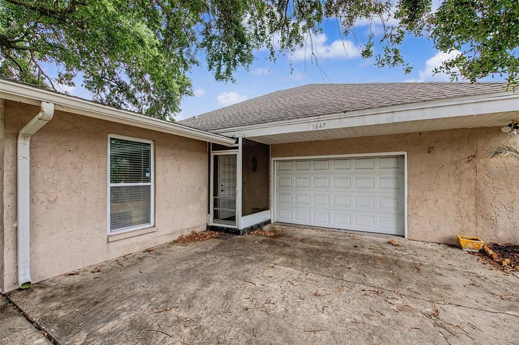 A tan stucco house exterior features a concrete driveway, a garage, and a screened entryway — 1647 SUMMERDALE DRIVE S, CLEARWATER, FL