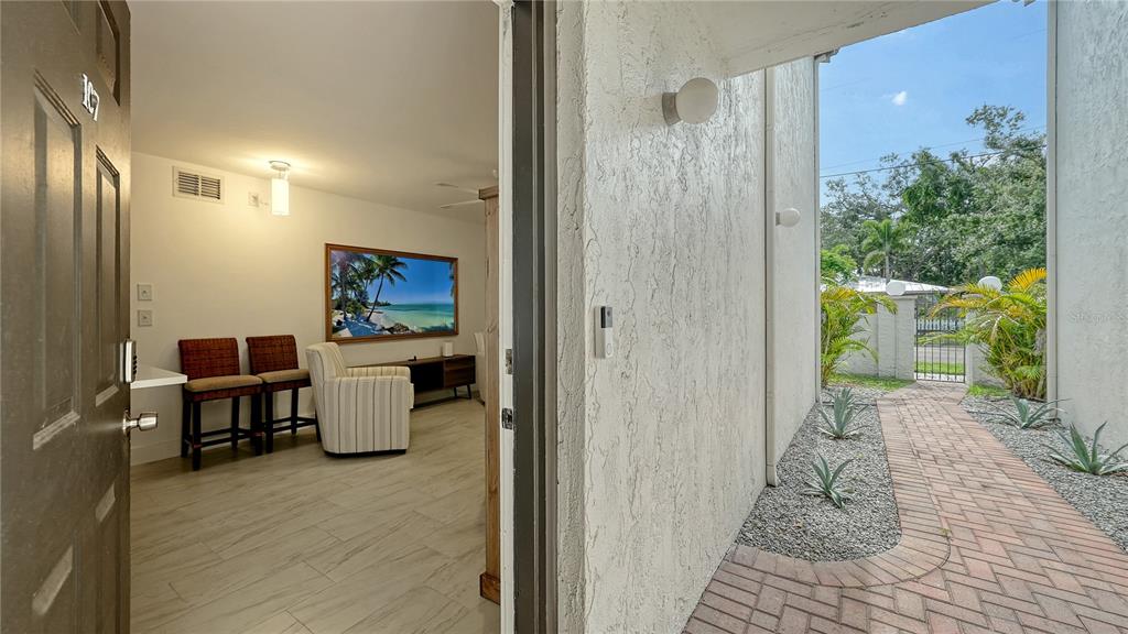 A view from an open doorway looking into a living room and a paved walkway — 631 N ORANGE AVENUE UNIT 107, SARASOTA, FL