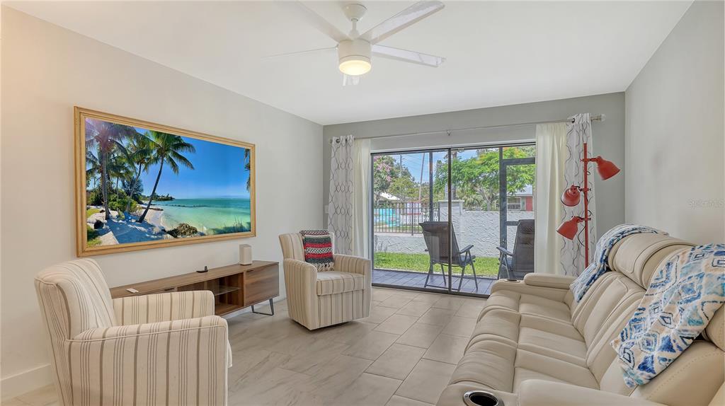 A living room features a beige sofa, two striped armchairs, a television, and sliding doors — 631 N ORANGE AVENUE UNIT 107, SARASOTA, FL