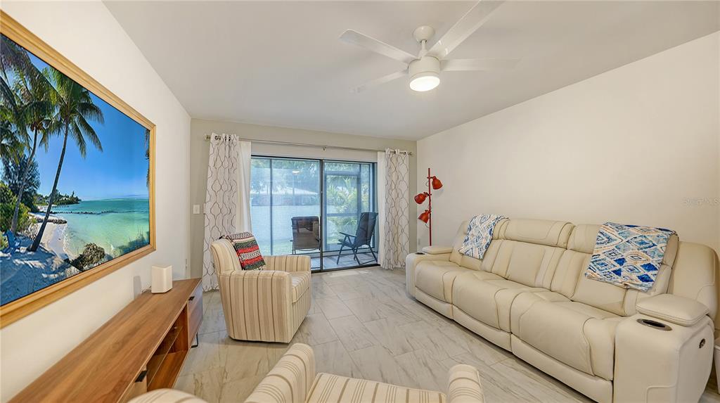 A living room features a white leather sofa, two patterned armchairs, and a large wall-mounted television — 631 N ORANGE AVENUE UNIT 107, SARASOTA, FL