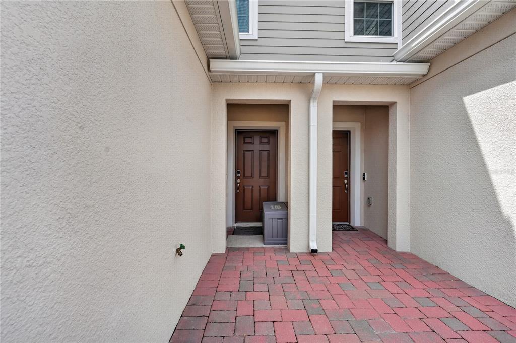 A paved entryway features two brown doors set into a stucco wall under a roofline — 1188 WOODY CYPRESS DRIVE, KISSIMMEE, FL