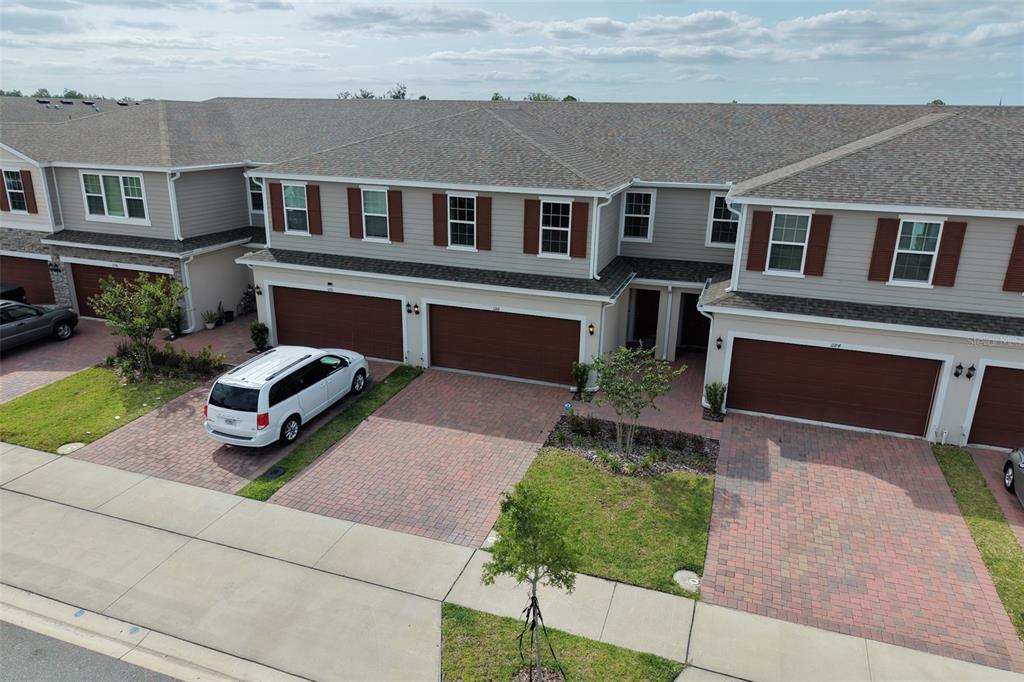 An aerial view shows a row of townhomes with brown garage doors and brick driveways — 1188 WOODY CYPRESS DRIVE, KISSIMMEE, FL