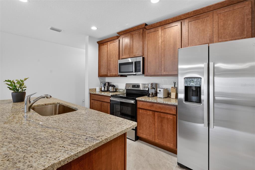 A kitchen features wood cabinets, granite countertops, stainless steel appliances, and a central island sink — 1188 WOODY CYPRESS DRIVE, KISSIMMEE, FL