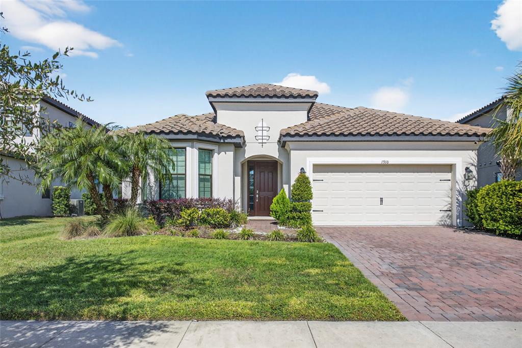 A single-story house with a tile roof, beige stucco exterior, and a brick paver driveway — 1910 GOBLET COVE STREET, KISSIMMEE, FL